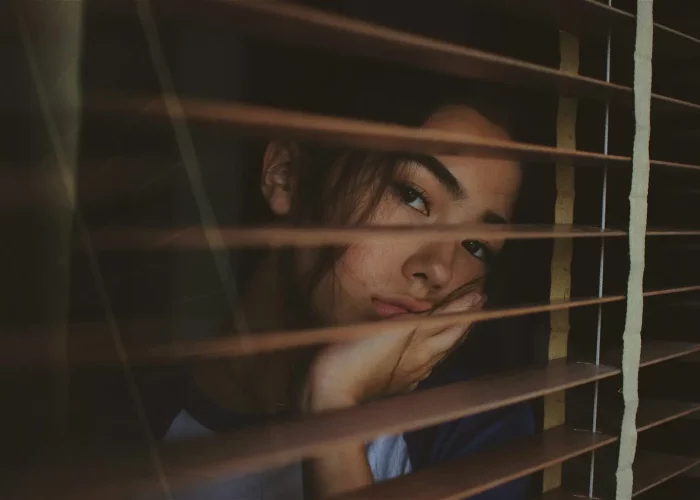 a woman looking out of a window with blinds